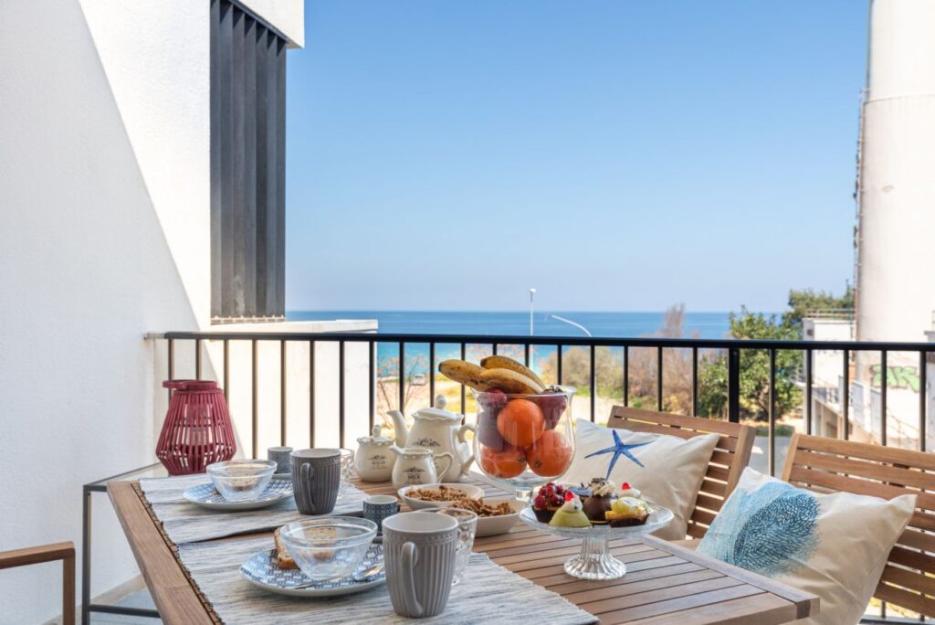 Cozy balcony seating with seaside cushions and breakfast table facing the open blue sea